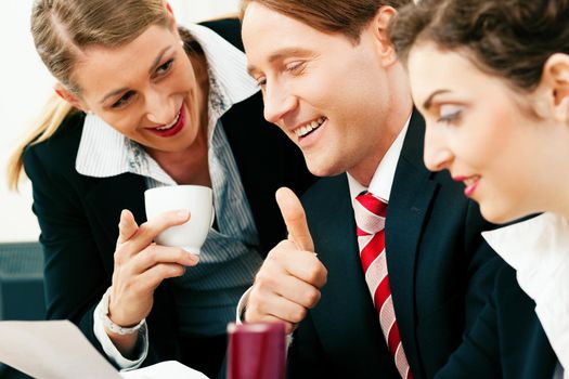 Small business team - man and two women - working in the office having a success, one woman drinking a mug of coffee