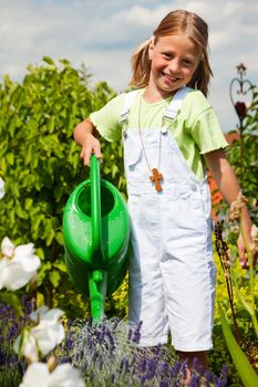 Little girl watering the flowers in a garden on a bright summer day