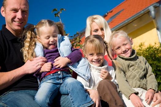 A young family with three children in front of their new home sitting in the sun