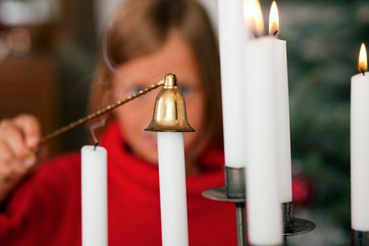 Child extinguishing Christmas candles in front of a Christmas tree