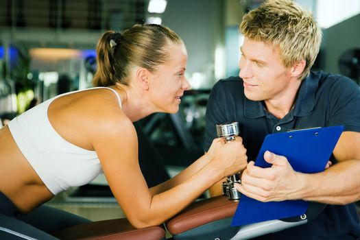 Woman with dumbbells in a gym, her personal trainer gives a report on her training