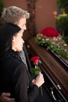 Morning man and woman on funeral with red rose standing at casket or coffin