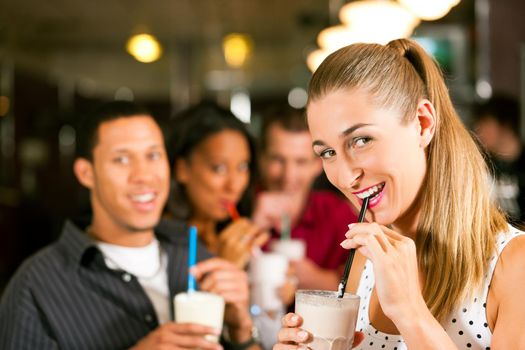 Friends drinking milkshakes in a bar and have lots of fun; focus on the woman in front