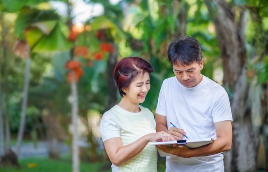 Asian middle-aged couple talking and designing garden plan together in backyard.