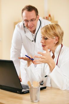 Two doctors - male and female - discussing test reports that show on their laptop screen