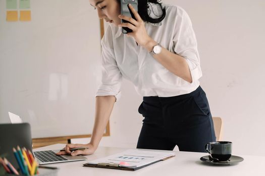 Young female entrepreneur working laptop computer and talking mobile phone to client.