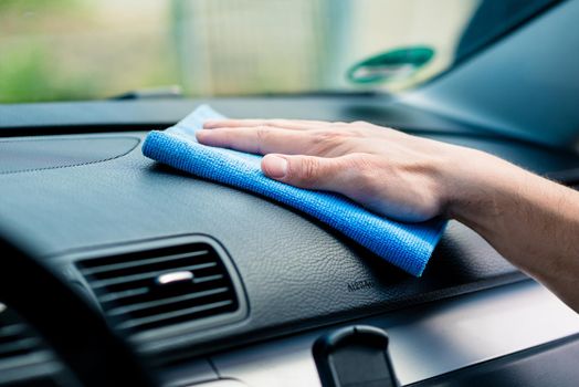 Man wiping the dashboard of his car with an anti-static cloth to remove accumulated dust, close up of his hand