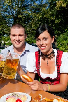 Couple in traditional Bavarian dress, Lederhosen and Dirndl, in a beer garden with Pretzel and Obatzter (traditional cheese)