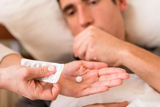 Sick man taking medication offered by a nurse who is holding a single pill in one hand and blister pack in the other