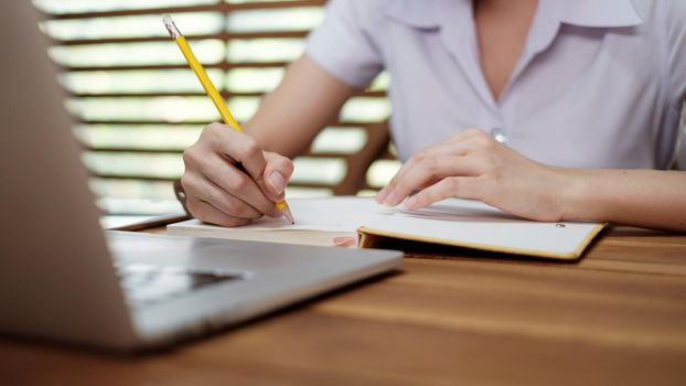 Young girl writing note with pen inspired ideas list on notepad while working on laptop computer, close up. woman attending online course on Elearning channel