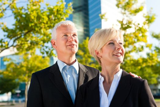 Business people - mature or senior - standing in a park outdoors in front of a office building