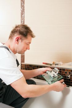 Plumber installing a mixer tap in a bathroom, he is sitting in the bathtub, focus on eyes of the man!