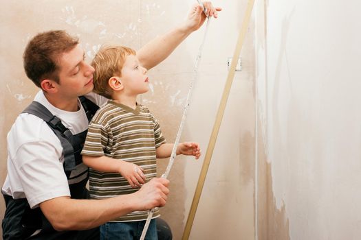 Father and son measuring a dry wall in their home with a folding rule and a bubble level
