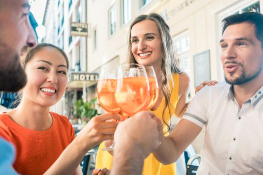 Low-angle view of a multi-ethnic group of four friends celebrating together with an orange refreshing summer drink at a trendy restaurant downtown