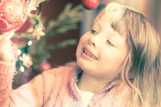 Young girl decorating the Christmas tree, holding some Christmas baubles in her hand being amazed by the festive atmosphere