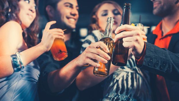 Group of party people men and women, with cocktails and beer bottles in a bar or club having fun