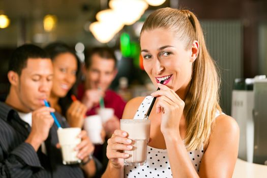 Friends drinking milkshakes in a bar and have lots of fun; focus on the woman in front