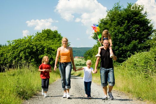 Family walking down a path on a bright summer day, a village in the background