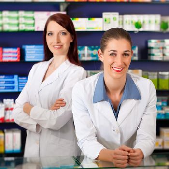 Pharmacist with female assistant in pharmacy standing in front of shelf with drugs