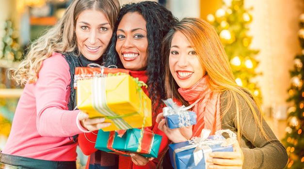 Group of three diversity women - white, black and Asian - with Christmas presents in a shopping mall in front of a Christmas tree