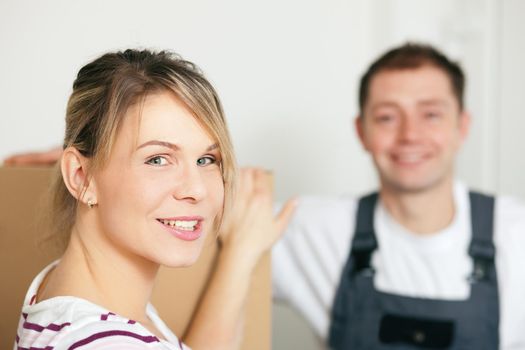 Woman moving in her new house, she is getting friendly help by a mover who is carrying the boxes