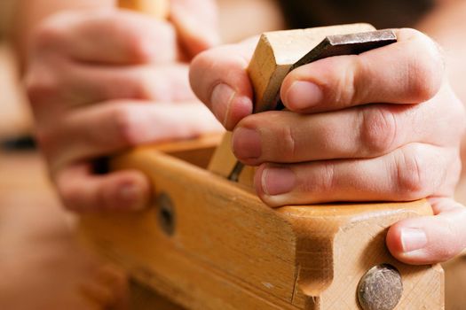 Carpenter working with a planer in his workshop, close up on the tool with hands