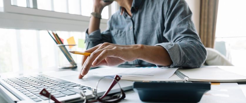 Young accountant hand holding smartphone to call marketing consultants and using laptop computer to analyze sales growth in the global workplace market. accounting concept.