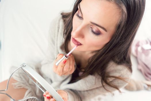 Woman applying lipstick in the morning on her bed