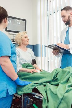 Doctor and nurse talking to patient in recovery room of hospital after she woke up from operation