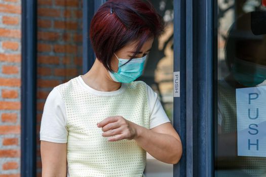 Woman wearing mask opening the door with the elbow for protection  infection COVID-19