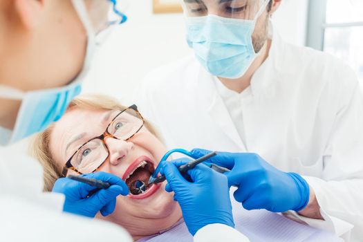 Dentist during treatment of senior patient woman looking into mouth