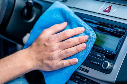 Man wiping the display glass on the dashboard in his car with a blue anti-static cloth as he cleans the vehicle, close up on his hand