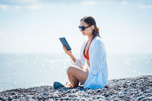 Woman reading a novel on ebook by the sea in her vacation