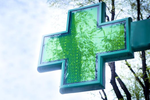 Green cross pharmacy symbol on blue sky background. No people