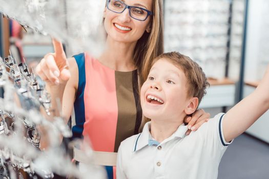 Mother and son both liking the eyeglasses offered in optician shop being excited 