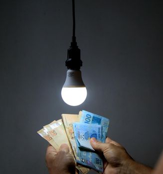 salvador, bahia / brazil - may 17, 2020: person counts money next to the led lamp lit in a residence in the city of Salvador.




