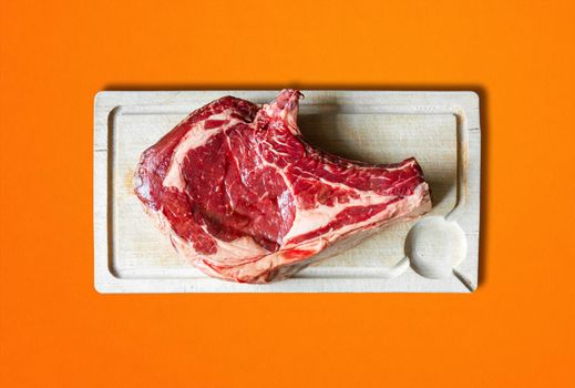 Raw beef prime rib on a cutting board. Orange background. Top view
