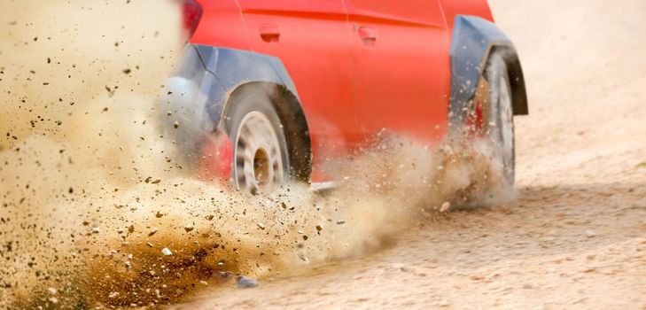 Gravel splashing from rally race car drift on track.