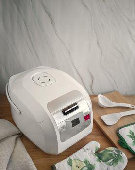 On the wooden table there is a modern electric multi cooker and kitchen accessories