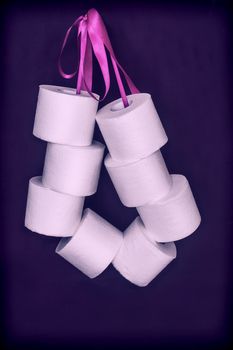 On a dark background, a roll of white toilet paper is connected by a ribbon in a bundle. Front view, vertical orientation