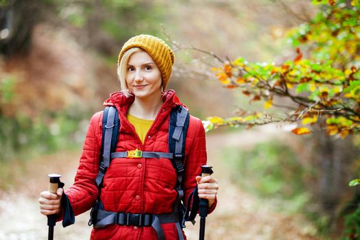 Hiking girl with poles and backpack standing on a trail. Looking at camera. Travel and healthy lifestyle outdoors in fall season