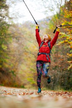 Hiking girl with poles and backpack on a trail. Hands up enjoying in nature. Travel and healthy lifestyle outdoors in fall season.