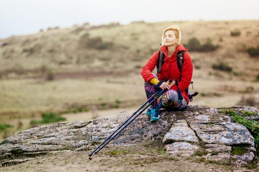 Hiker girl taking a rest on a rock in the mountains. Windy day. Travel and healthy lifestyle outdoors in fall season