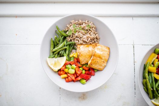 Top view of salmon and buckwheat dish with green beans, broad beans, and tomato slices. Nutritious dishes with vegetables and fish from above. Healthy balanced diet