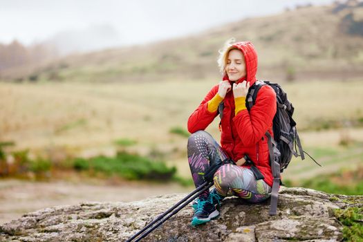 Hiker girl taking a rest on a rock in the mountains. Windy day. Travel and healthy lifestyle outdoors in fall season