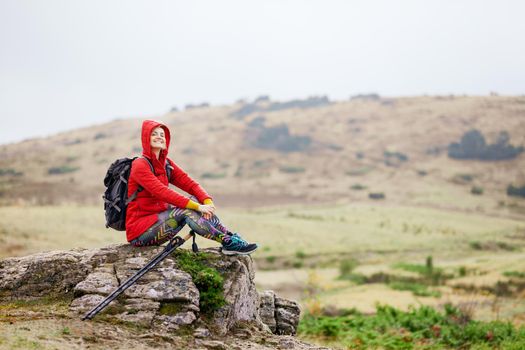 Hiker girl taking a rest on a rock in the mountains. Windy day. Travel and healthy lifestyle outdoors in fall season