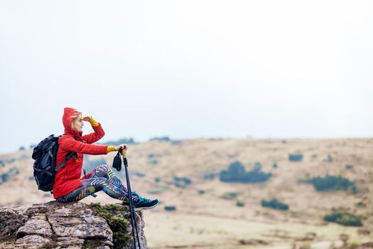 Hiker girl taking a rest on a rock in the mountains. Enjoying the view. Travel and healthy lifestyle outdoors in fall season