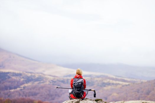 Hiker girl taking a rest on a rock in the mountains. Windy day. Travel and healthy lifestyle outdoors in fall season