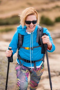 Hiking girl with poles and backpack standing on rocks. Windy autumn day. Travel and healthy lifestyle outdoors in fall season