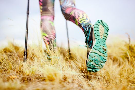 Hiking girl in a mountain meadow. Low angle view of generic sports shoe and legs on grass. Healthy fitness lifestyle outdoors.